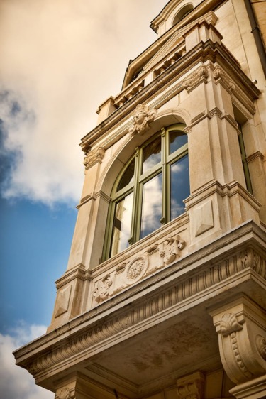 Architectural detail of an ornate building with large windows and decorative stonework set against a partly cloudy sky.