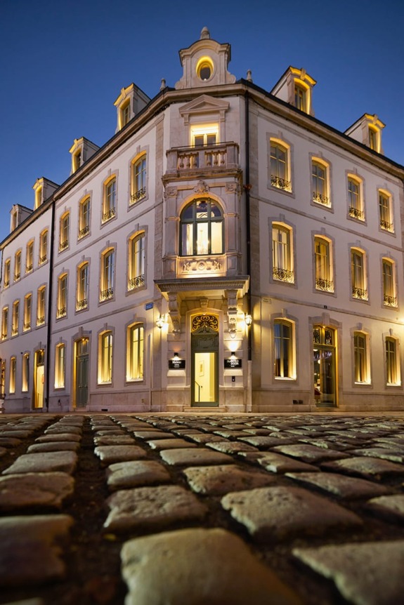 Elegant building with illuminated windows at dusk, viewed from a cobblestone street corner.