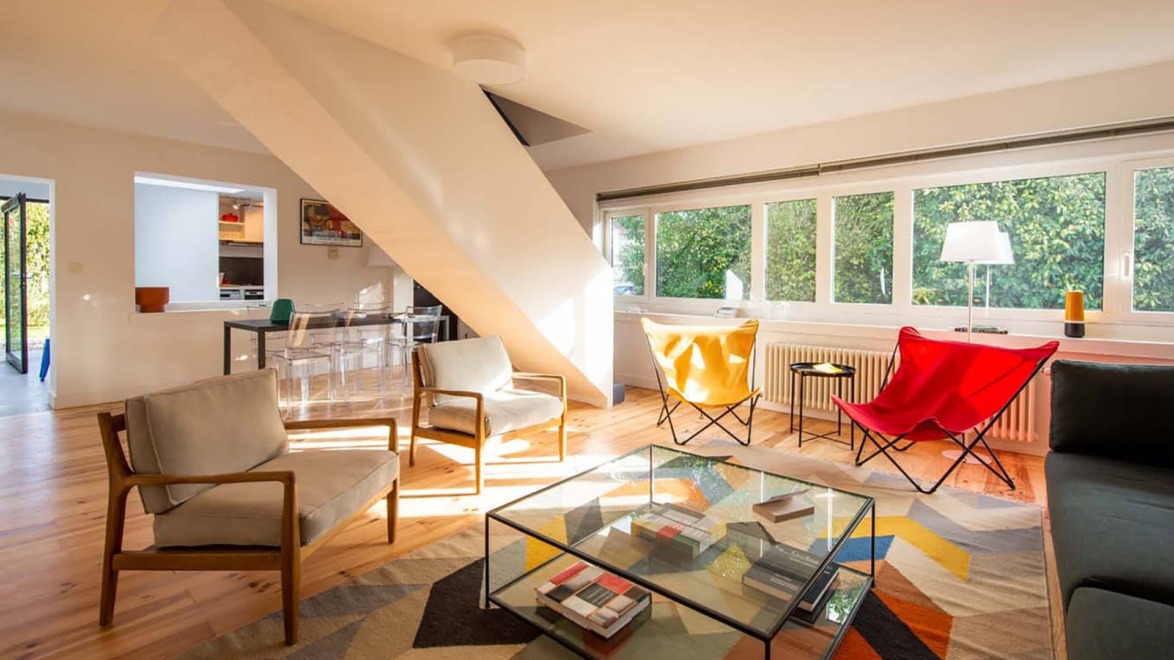 Modern living room with colorful chairs, glass coffee table, and large windows letting in natural light.