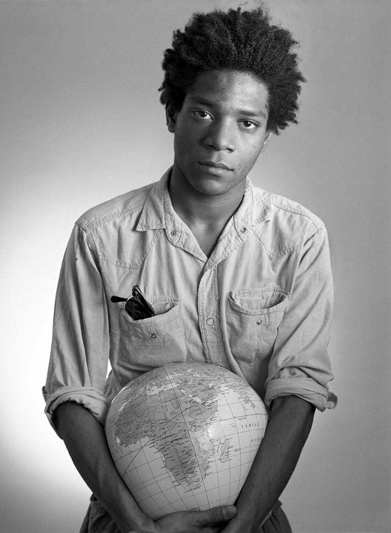 Person holding a globe against a plain background, wearing a button-up shirt with sunglasses in the pocket.