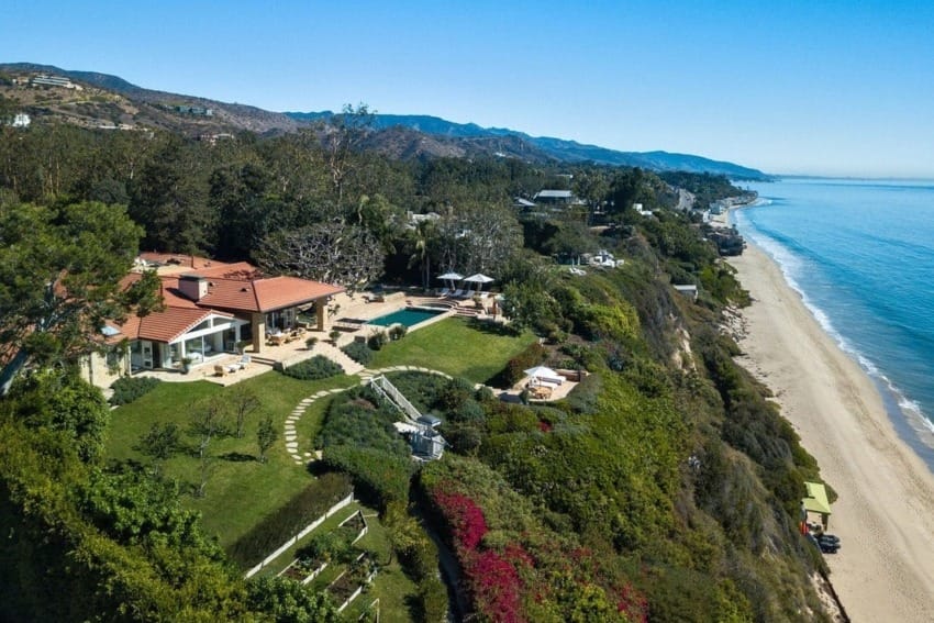 Aerial view of a coastal home with a pool and garden overlooking a beach and ocean.