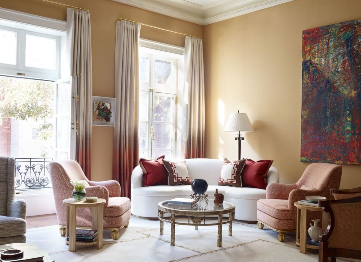 Elegant living room with a white sofa, pink chairs, large abstract painting, and tall windows with beige curtains.