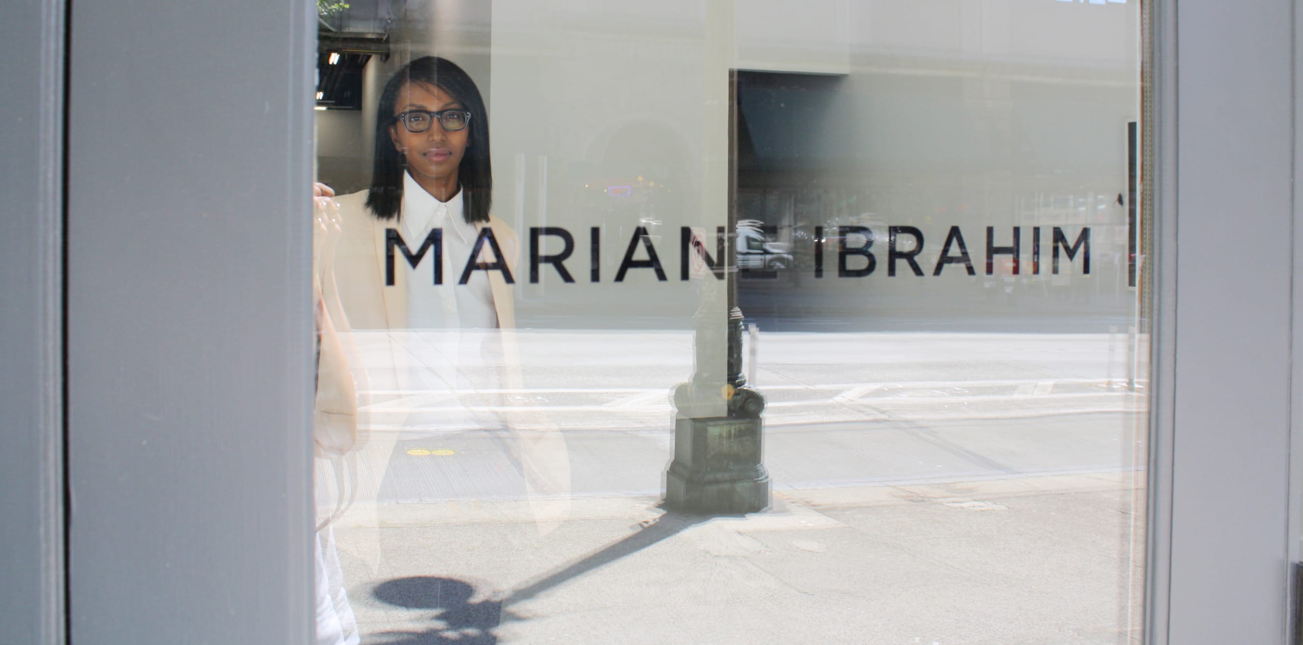 Person looking through a gallery window with the text "Mariane Ibrahim" on the glass in an urban setting.