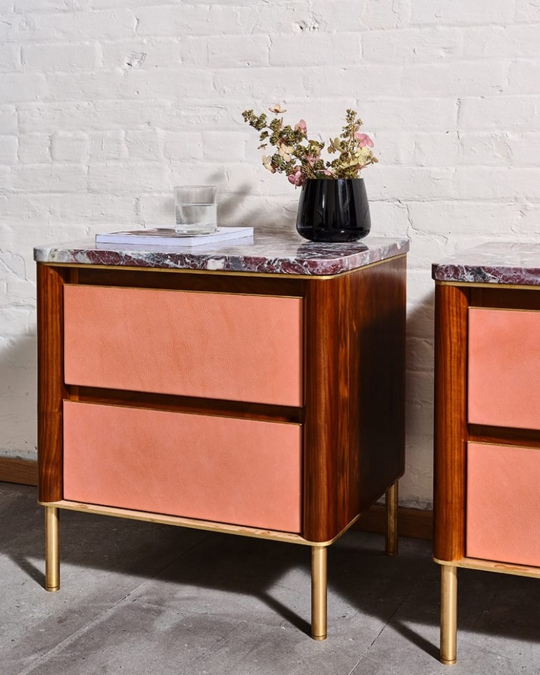 Mid-century modern side table with marble top and pink drawers, decorated with a vase and book, against a white brick wall.