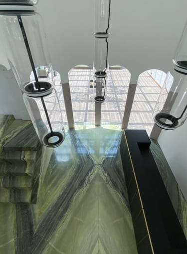 View of modern glass pendant lights and polished green marble floors with large arched windows in a stylish interior space