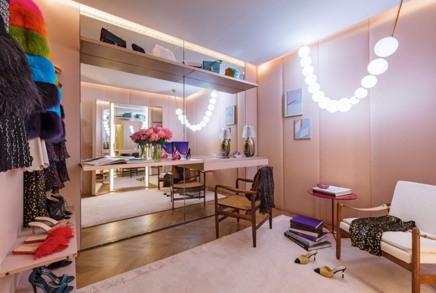 Luxurious dressing room with pink walls, elegant lighting, mirrored vanity, and stylish decor accents, including flowers and art.