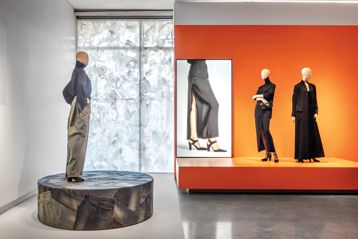 Fashion display with mannequins wearing stylish, modern outfits in a bright showroom featuring an orange accent wall.