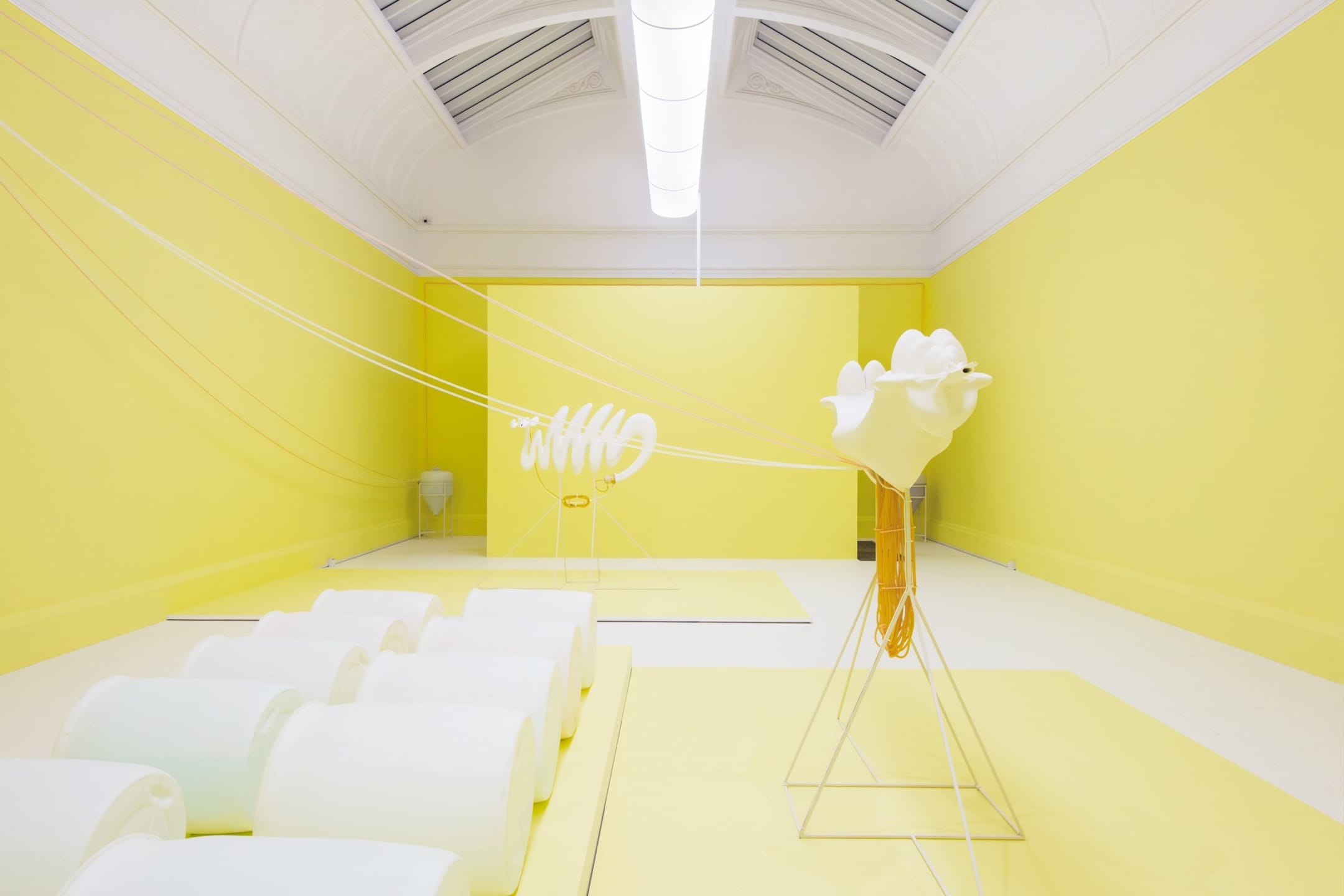 A brightly lit contemporary art installation with abstract yellow and white sculptures in a spacious gallery room.