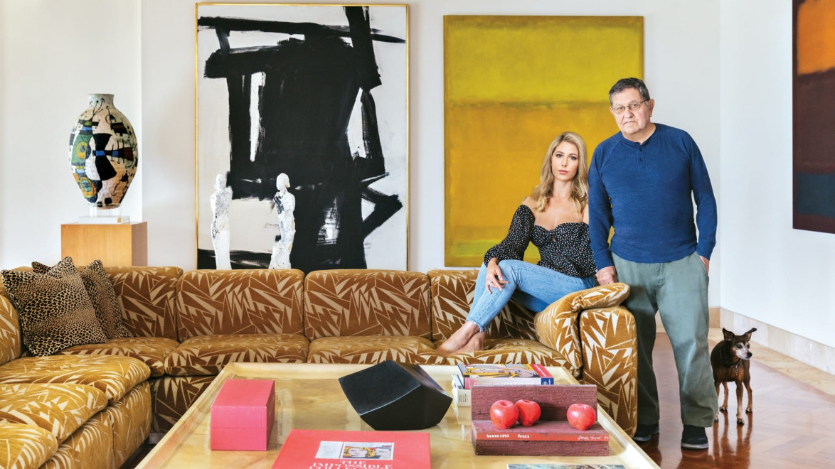 Two people in a modern living room with abstract art, patterned sofa, and wooden flooring.