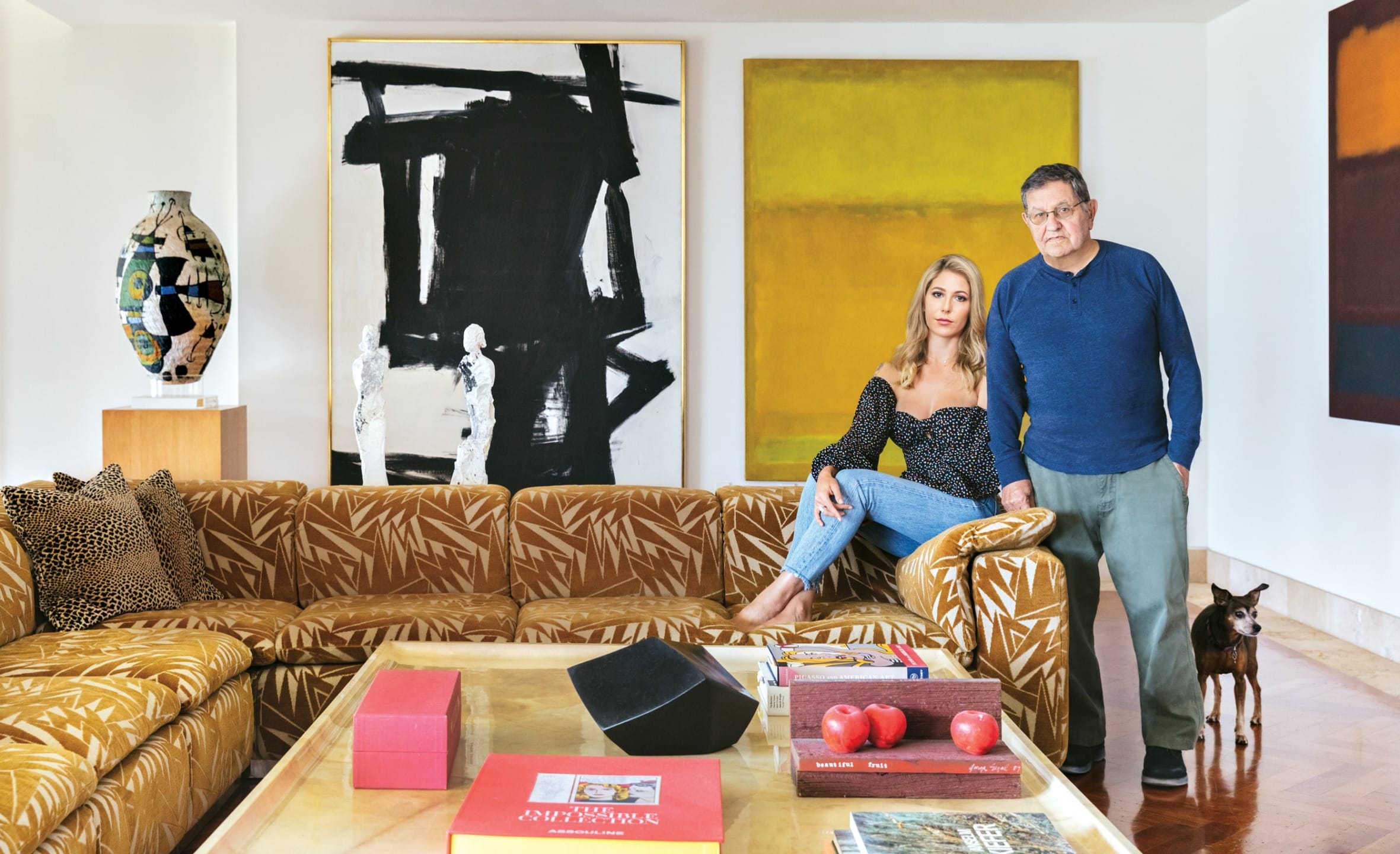 Two people in a modern living room with abstract art, patterned sofa, and wooden flooring.
