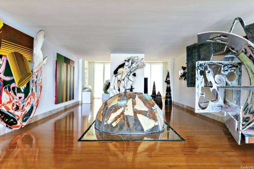Contemporary art sculptures and paintings on display in a spacious gallery with a reflective wooden floor.
