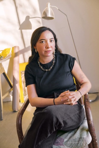Person sitting on a chair in a sunlit room with a lamp in the background.