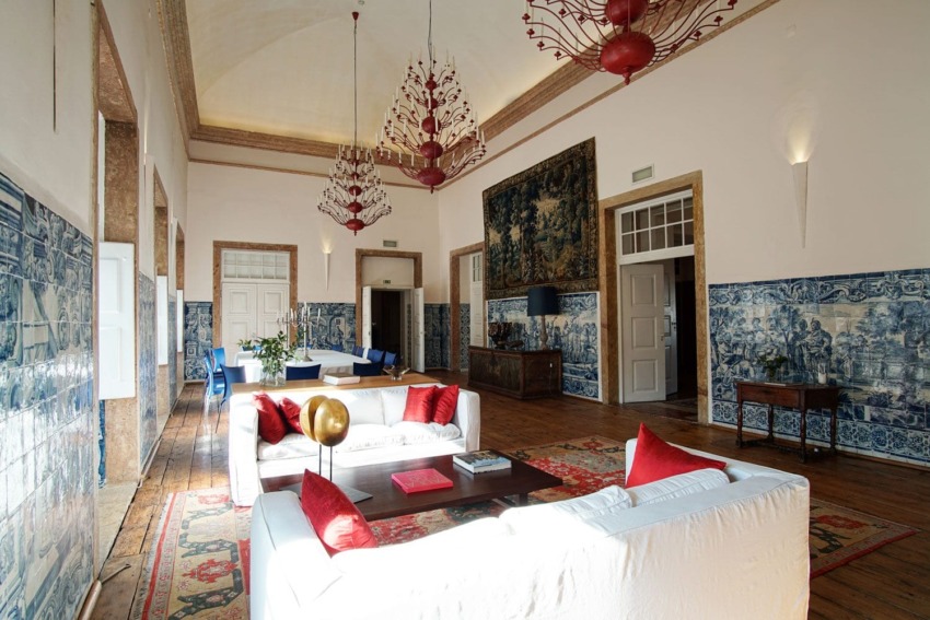 Elegant living room with white sofas, red cushions, ornate chandeliers, blue and white wall tiles, and wooden flooring.