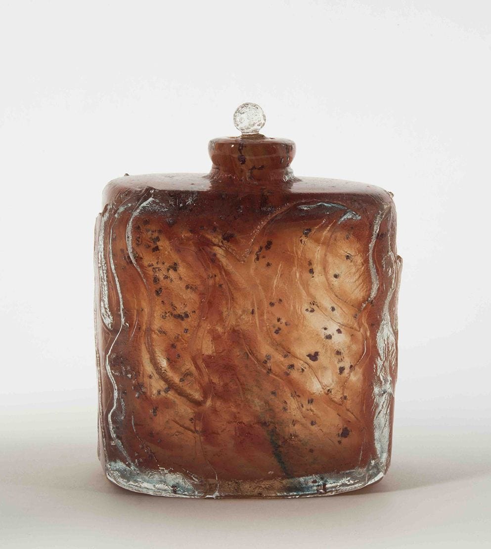 Antique brown glass bottle with a round stopper, featuring swirling patterns and slight weathering against a white background.