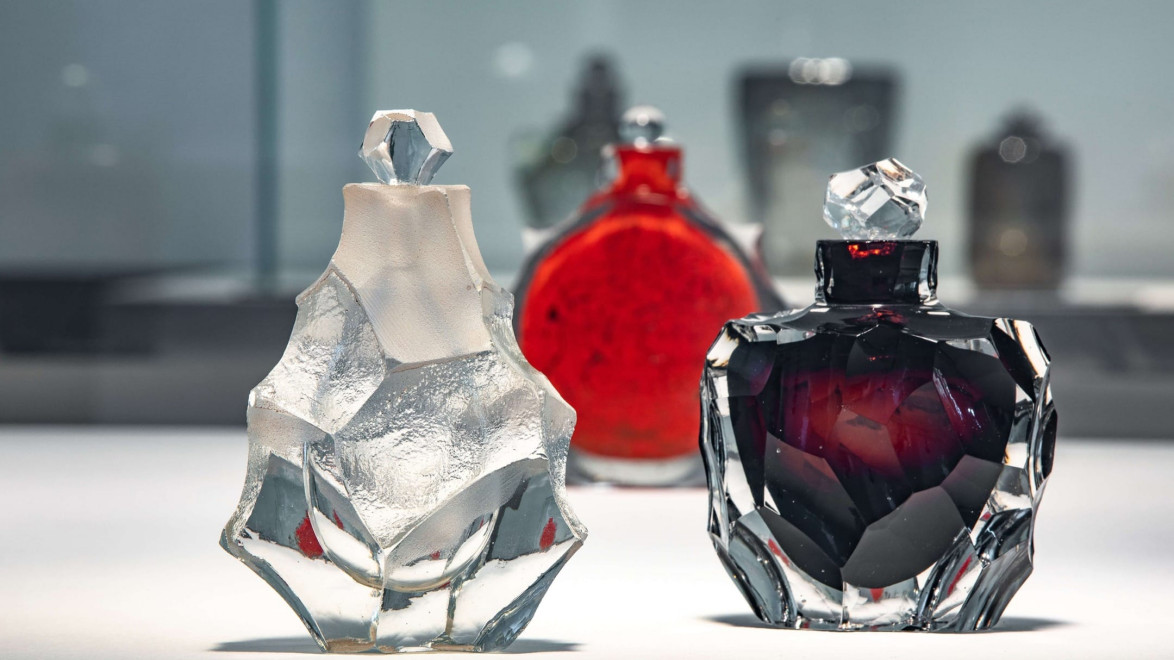 Three elegant crystal perfume bottles with intricate designs on a reflective surface, against a blurred background.