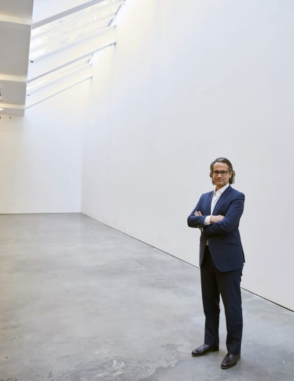 Man in a suit standing confidently in a spacious, modern art gallery with minimalist design and natural lighting.