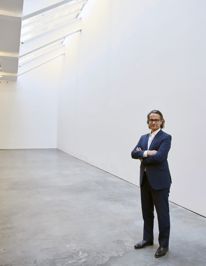 Man in a suit standing confidently in a spacious, modern art gallery with minimalist design and natural lighting.