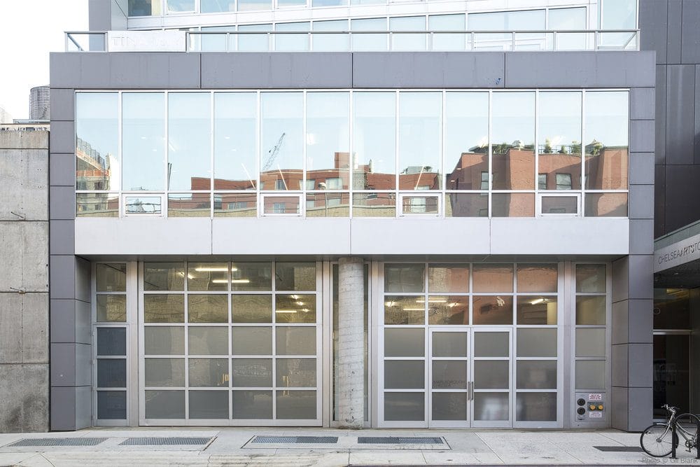 Modern building facade with large glass windows reflecting urban landscape, and a bicycle parked nearby on a city street.