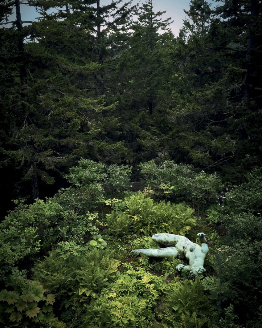 Statue of a giant hand partially buried in lush green forest surrounded by dense trees and foliage.