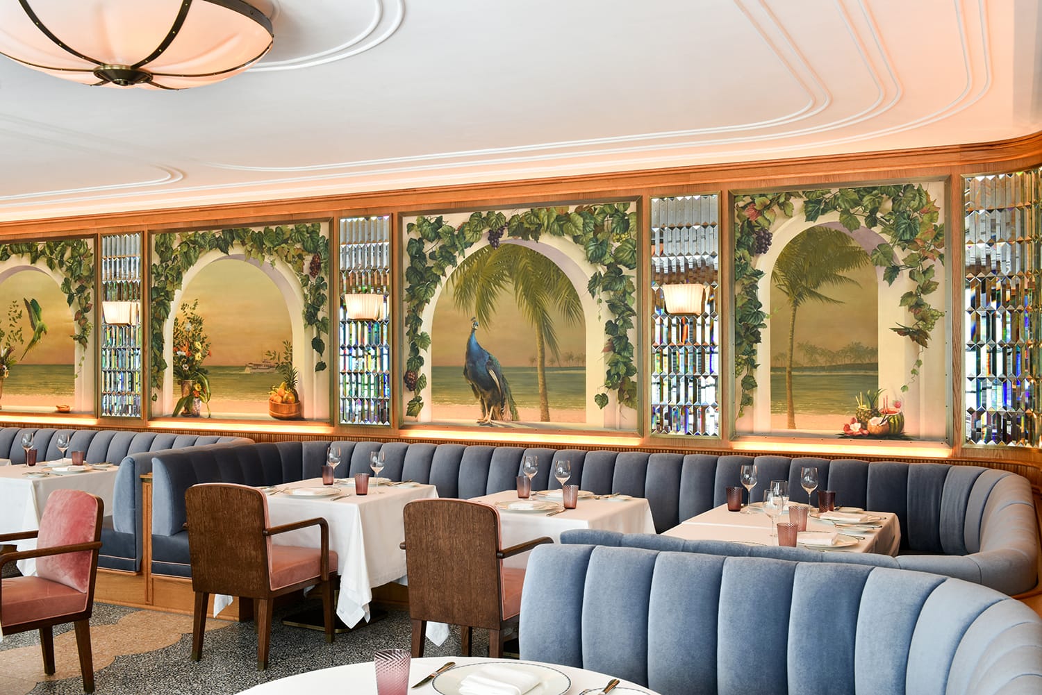 Elegant restaurant interior with blue booths, white tablecloths, and tropical-themed murals on the walls.