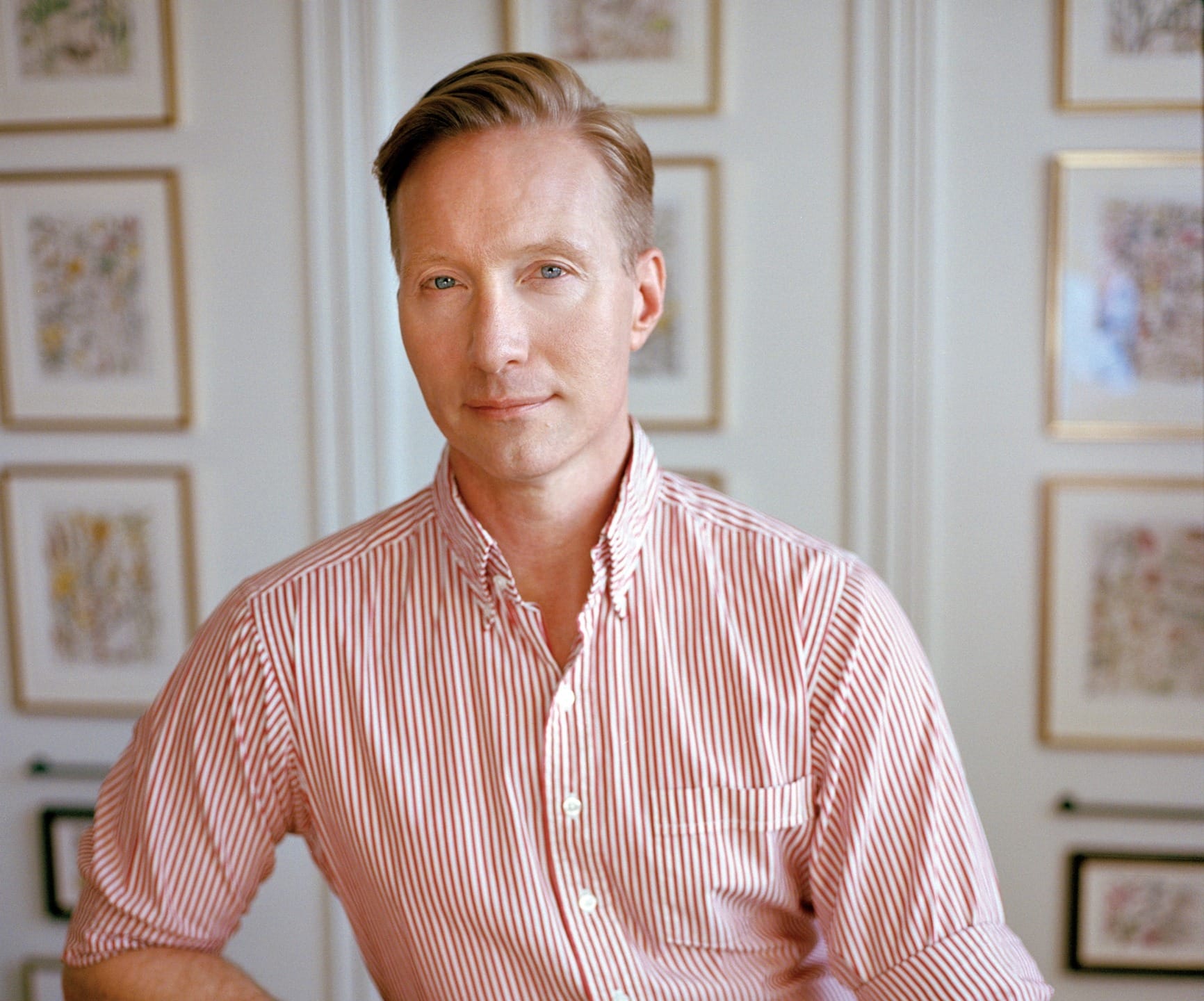 Person in a red and white striped shirt poses in front of framed artwork on a wall.