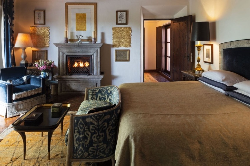 Cozy bedroom with a fireplace, elegant armchairs, a luxurious bed, and warm lighting creating a relaxing ambiance.