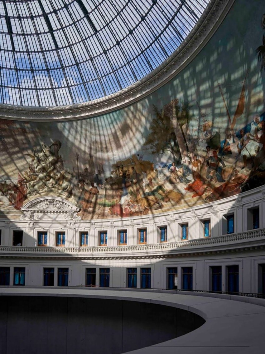 Spacious interior with a large glass dome and an intricately painted mural on the curved wall above rows of windows.