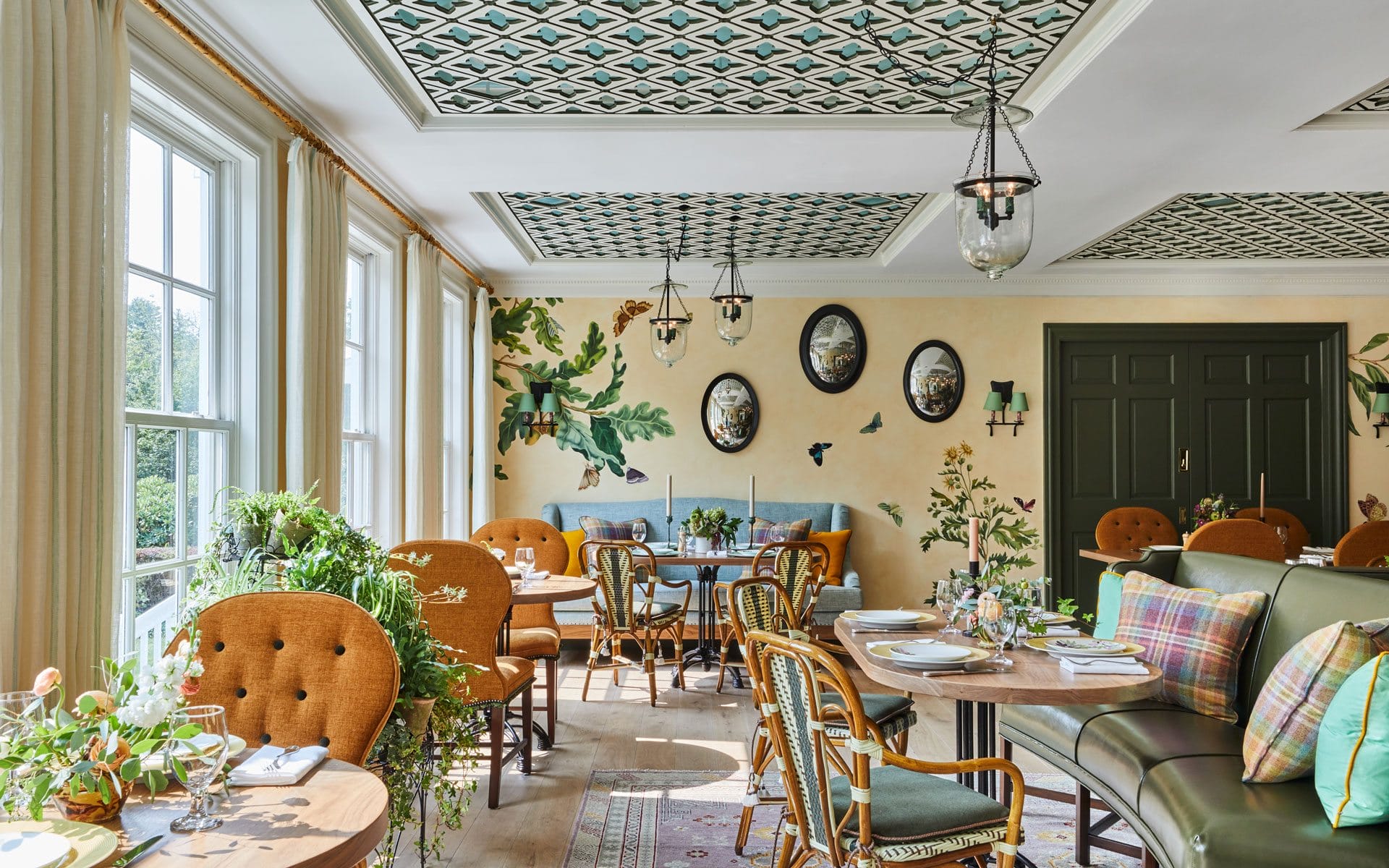 Bright restaurant interior with patterned ceiling, cozy seating, green plants, and decorative wall plates.