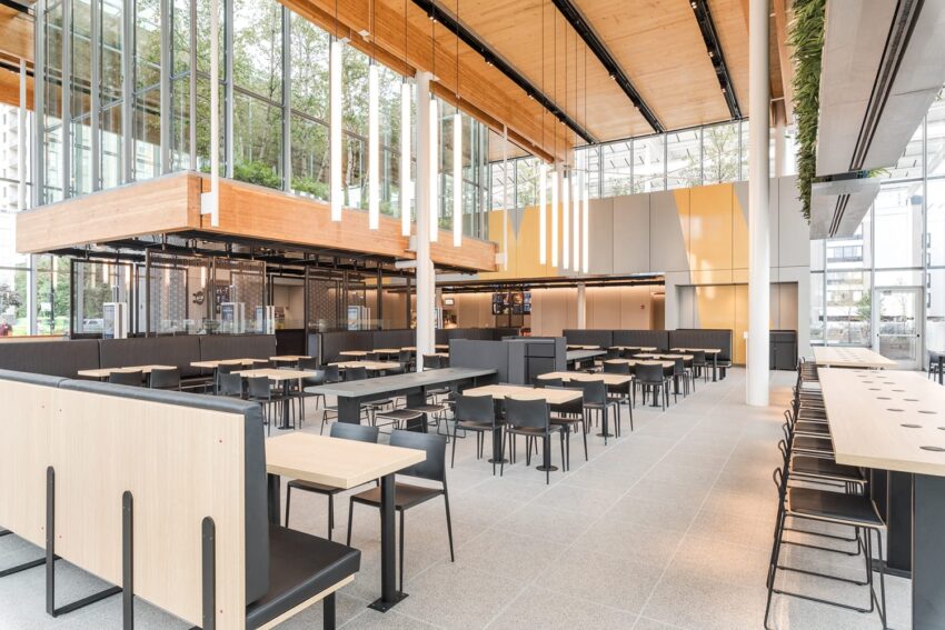 Modern cafeteria with wooden accents, large windows, and black seating in a bright, spacious dining area.