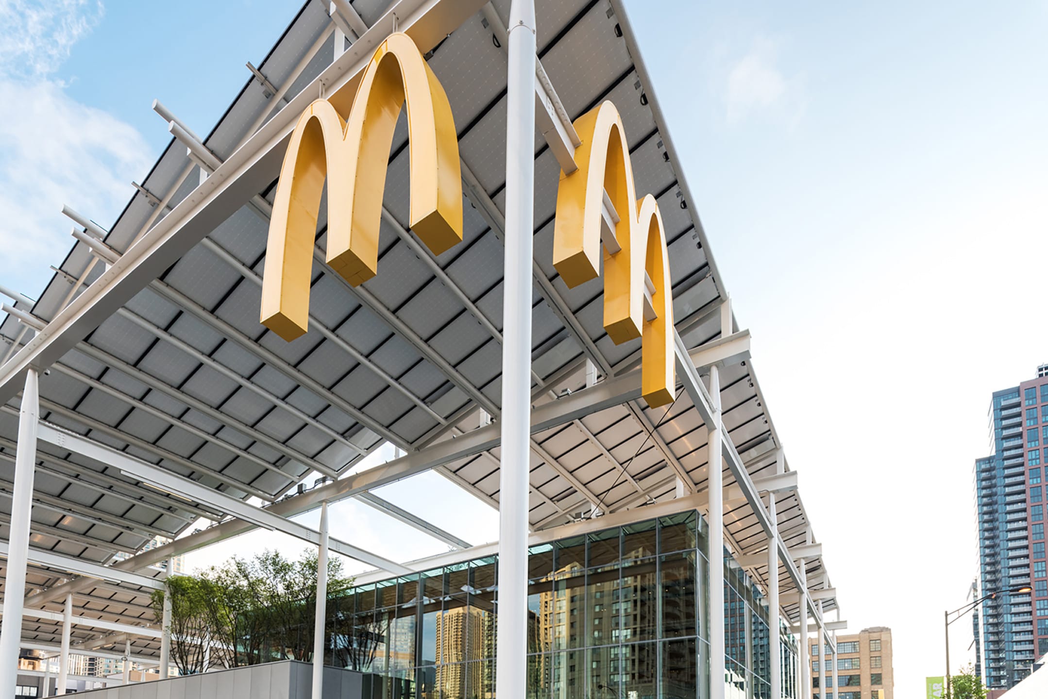 Modern McDonald's with solar panels on roof, surrounded by high-rise buildings and clear blue sky.