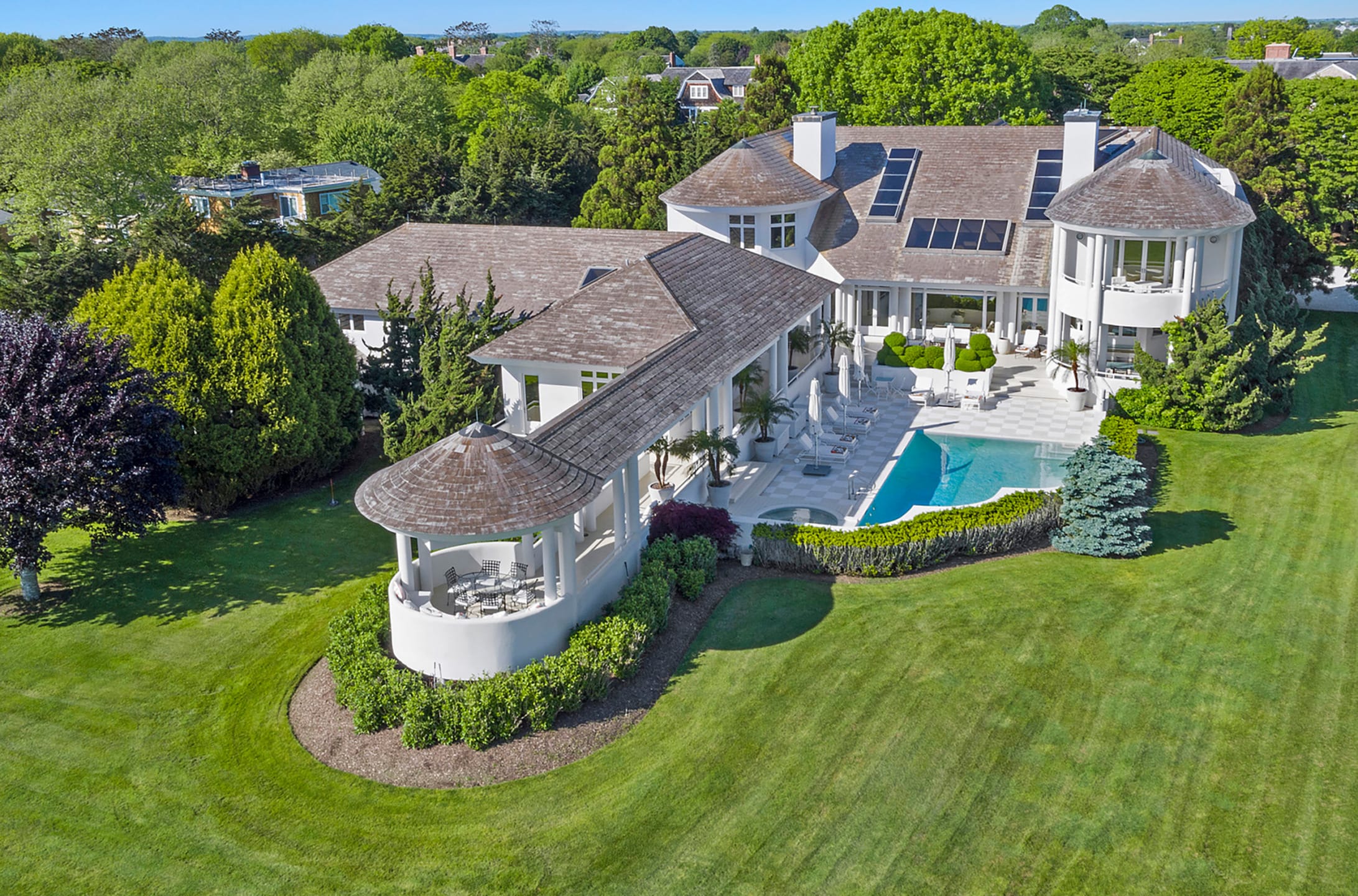 Aerial view of a large luxury mansion with pool and landscaped garden surrounded by lush green trees.