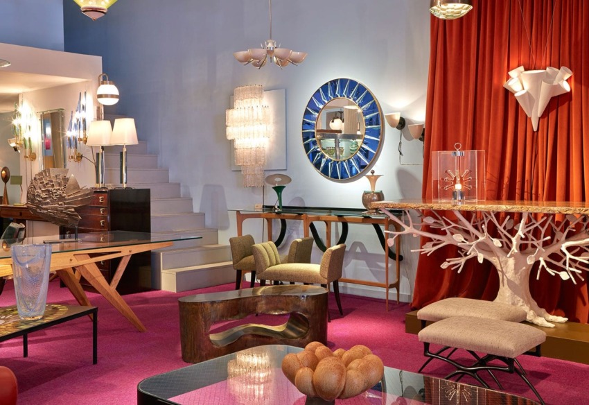 Vintage furniture store interior with eclectic decor, featuring mirrors, chairs, tables, unique lighting, and a pink carpet.