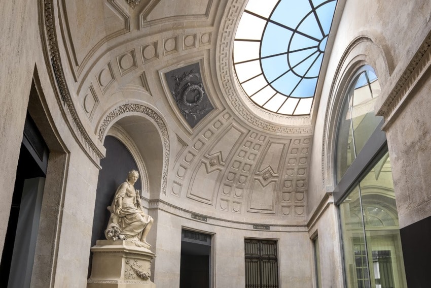 Decorative stone statue inside historical building with arched ceiling and glass dome, showcasing architectural details.
