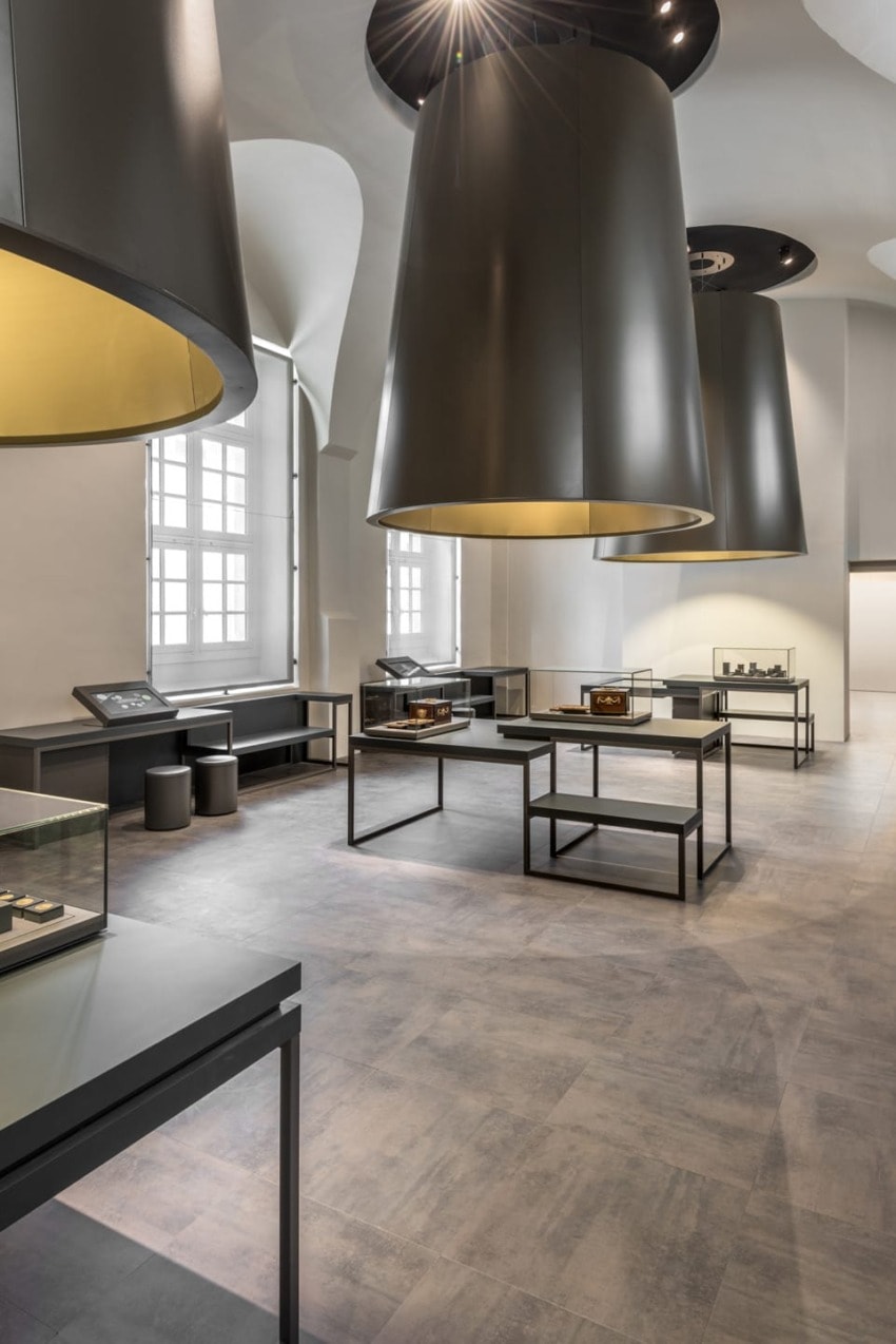 Modern exhibition room with large black cylindrical lights, glass display cases, and grey tiled flooring.