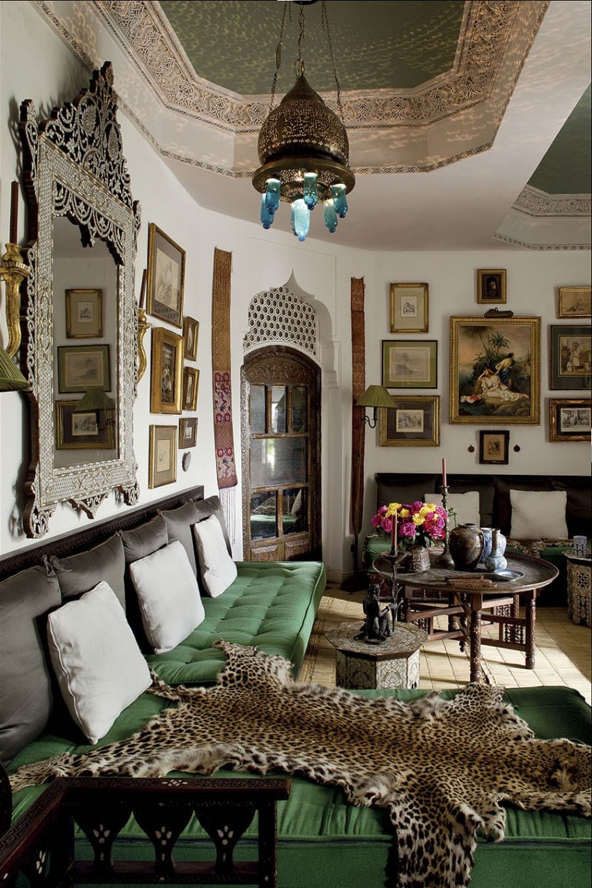 Luxurious Moroccan living room with ornate decor, green seating, decorative mirrors, artwork, and a colorful hanging lamp.