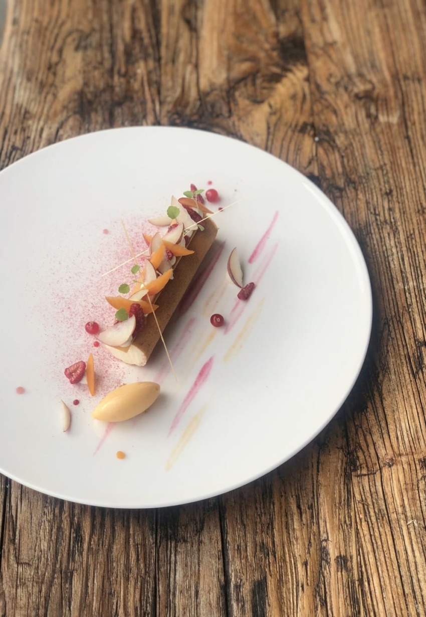Elegant dessert with artistic presentation on a white plate, featuring colorful garnishes and sauces on a rustic wooden table.