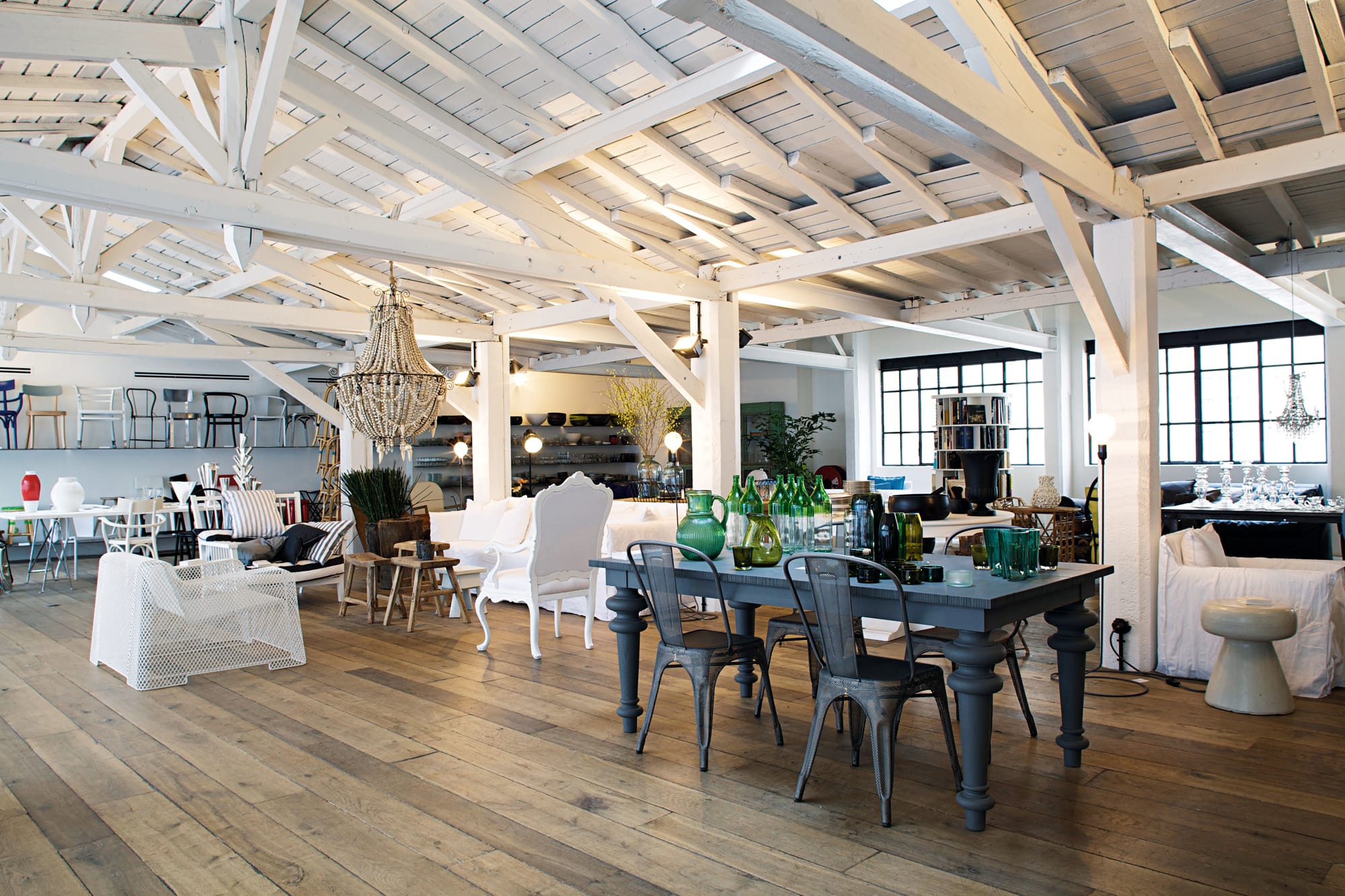 Spacious open-plan loft with wooden beams, large windows, eclectic furniture, and a mix of industrial and vintage decor.