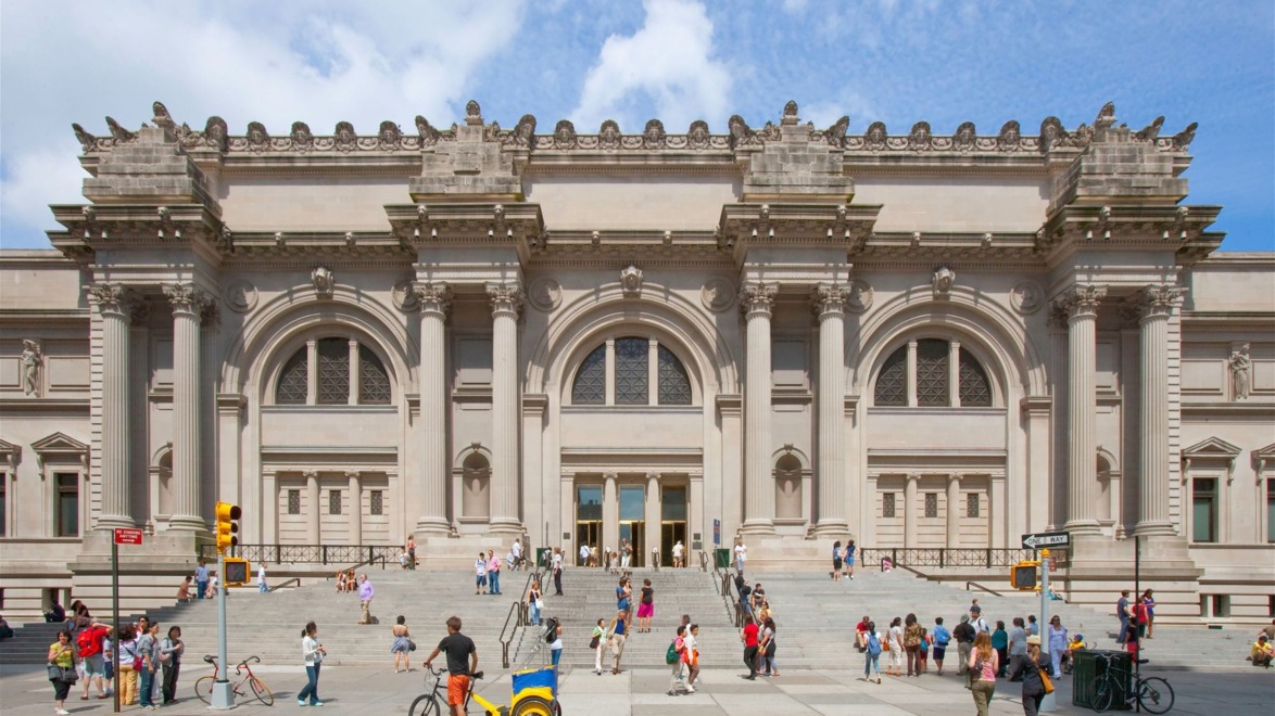 Exterior view of a large museum with a grand entrance and ornate architectural details, people walking in front.