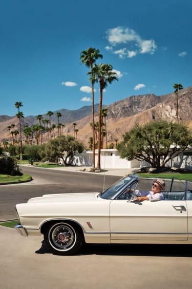 Classic convertible car parked on sunny desert road with palm trees and mountains in the background