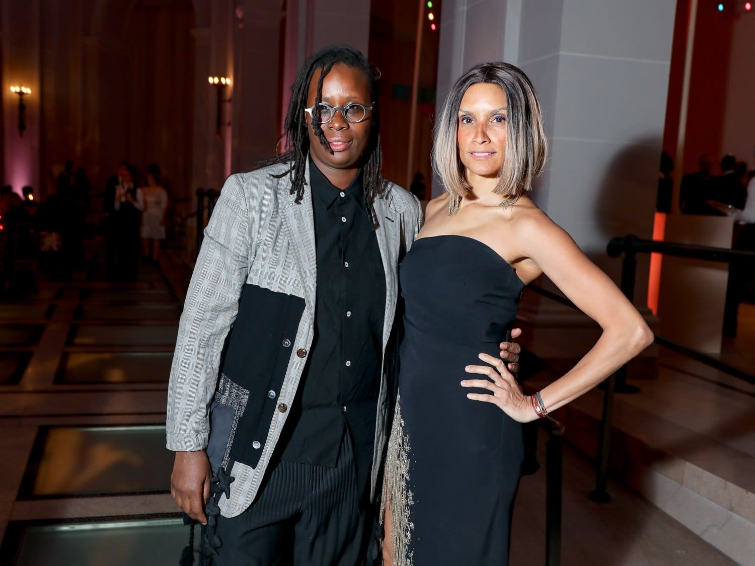 Two people posing and smiling at a formal event with elegant attire and a softly lit background.
