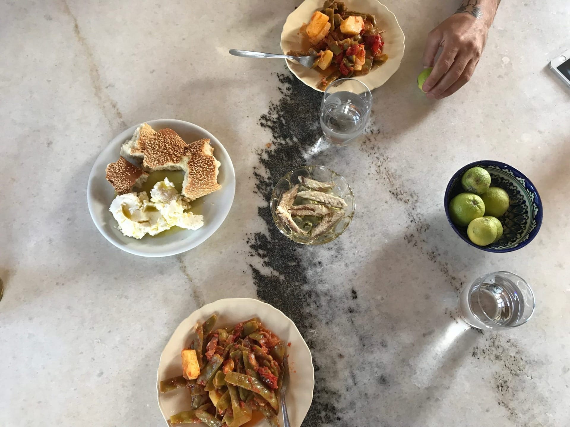 Table with various dishes including vegetables, bread with cheese, a bowl of limes, and glasses of water.