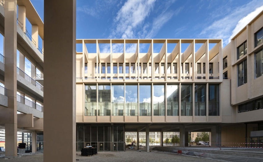 Modern building with large glass windows and architectural frames, under a blue sky with scattered clouds.