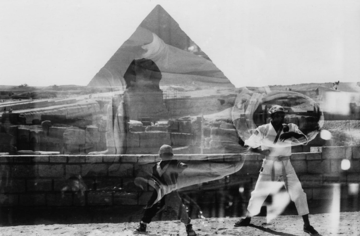 Martial arts practice by two people near the Pyramid of Giza, with a layered reflective effect in the image.