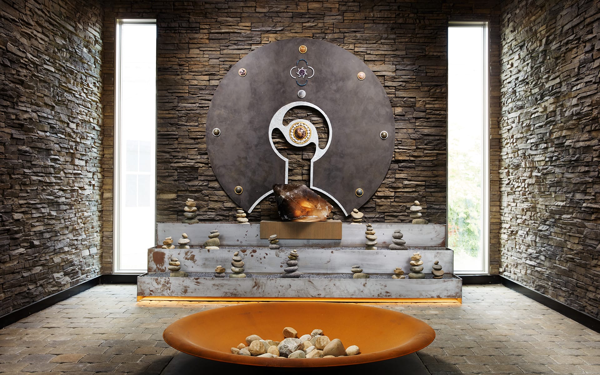 Modern meditation room with a large stone wall feature, round metal art, and a shallow bowl filled with stones.