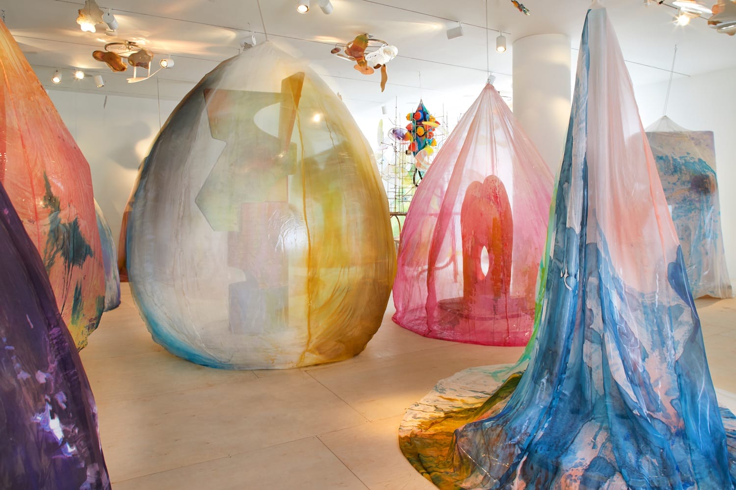 Colorful, translucent textile art installations hanging in a bright gallery space.
