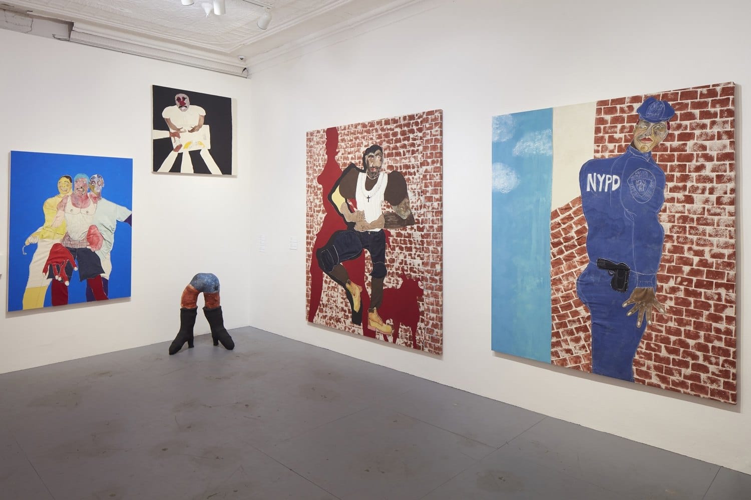 Art gallery interior displaying street art paintings, including figures and a police officer, on brick wall backdrops.