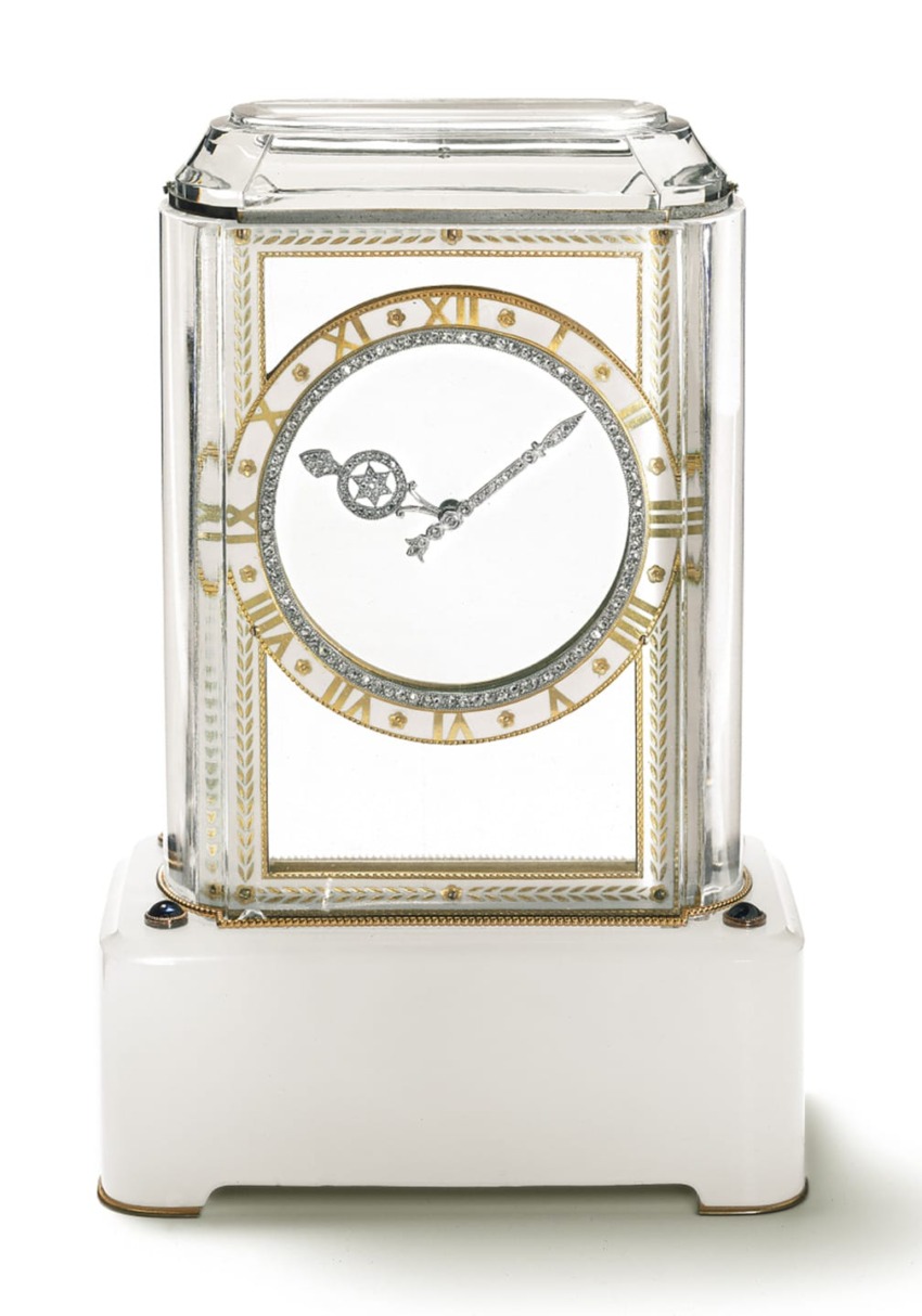 Elegant glass clock with gold and silver accents, roman numerals, and intricate hands on a white pedestal base.