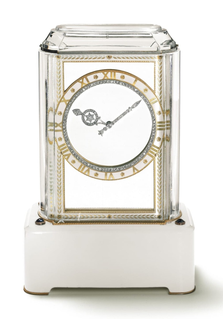 Elegant glass clock with gold and silver accents, roman numerals, and intricate hands on a white pedestal base.
