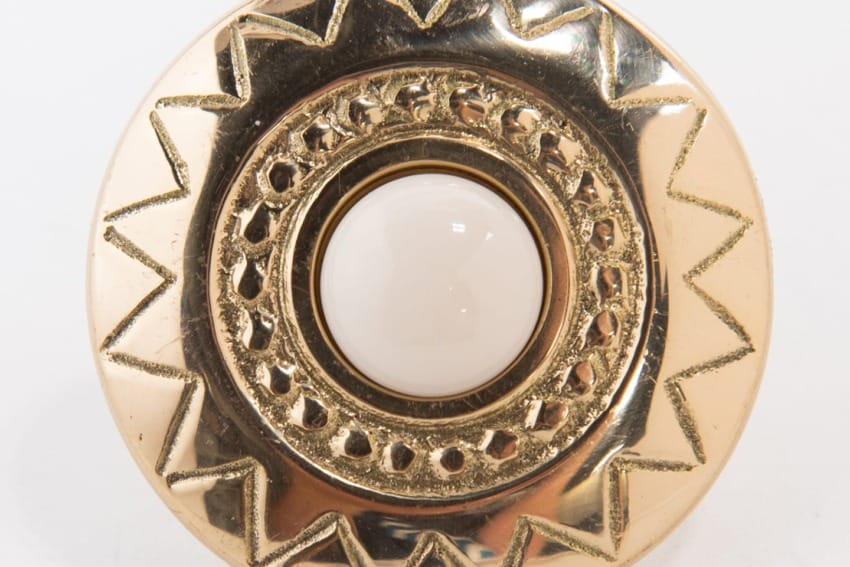 Gold round button with intricate zigzag pattern and white central inlay.