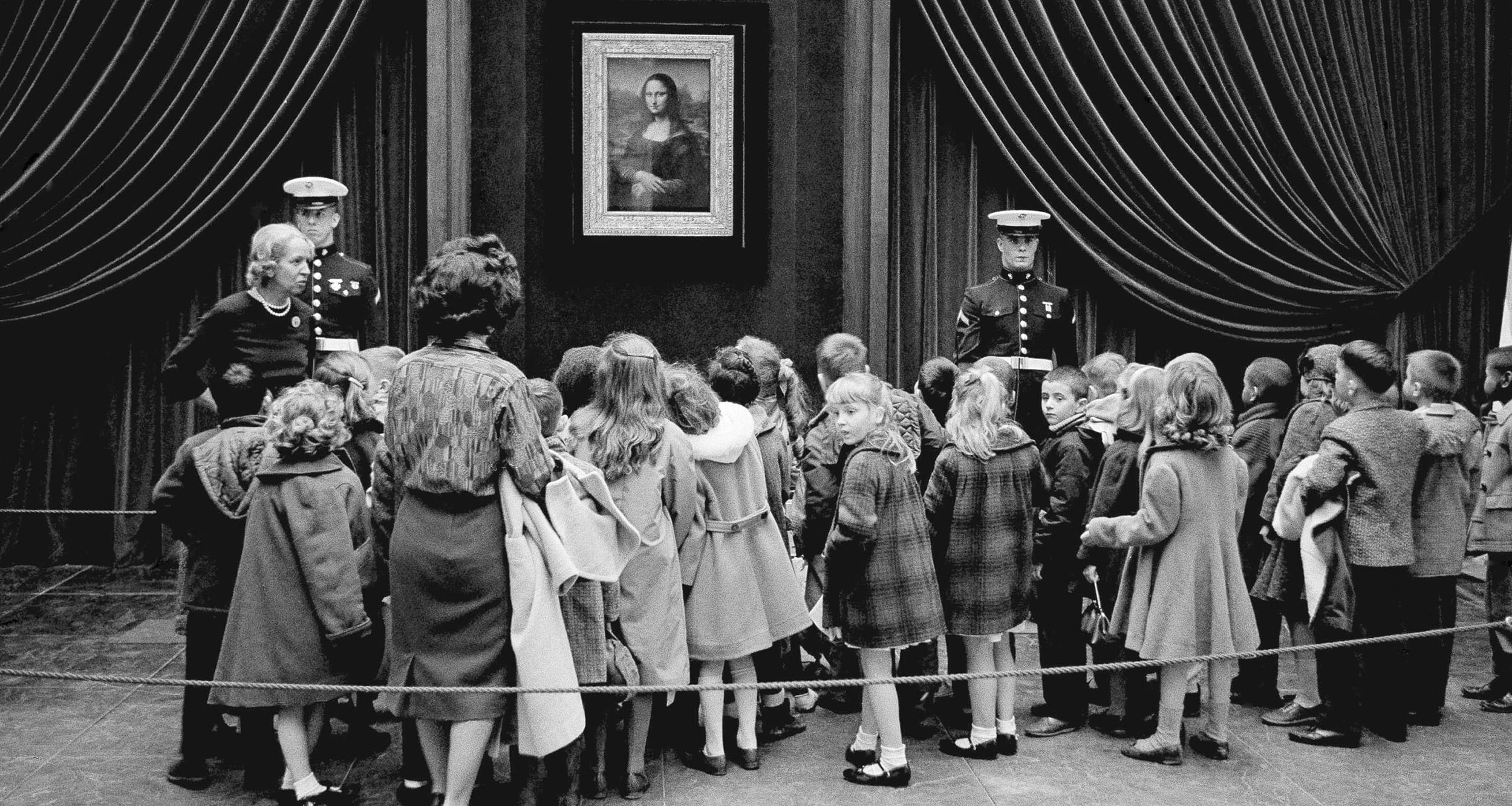 Children view the Mona Lisa painting displayed in a gallery with two guards and an audience in black and white.